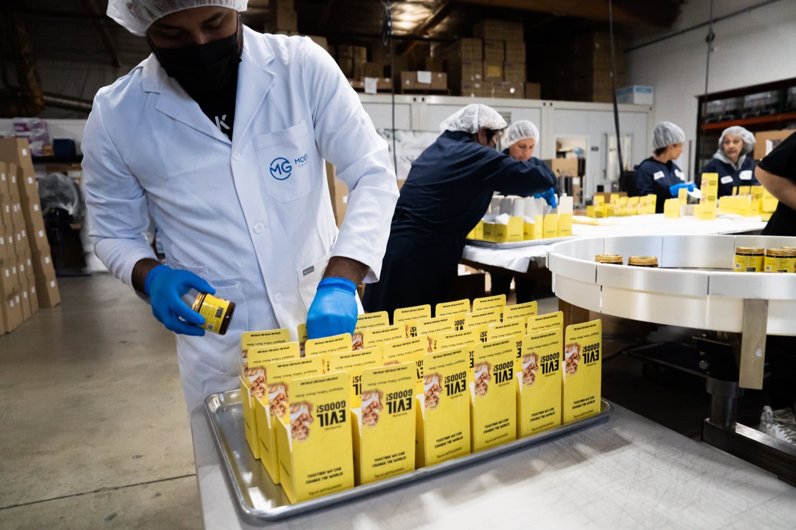 Moe’s Group production staff in branded lab coats, hairnets and gloves packing cartons beside a rotary filling line at the Chatsworth, California facility