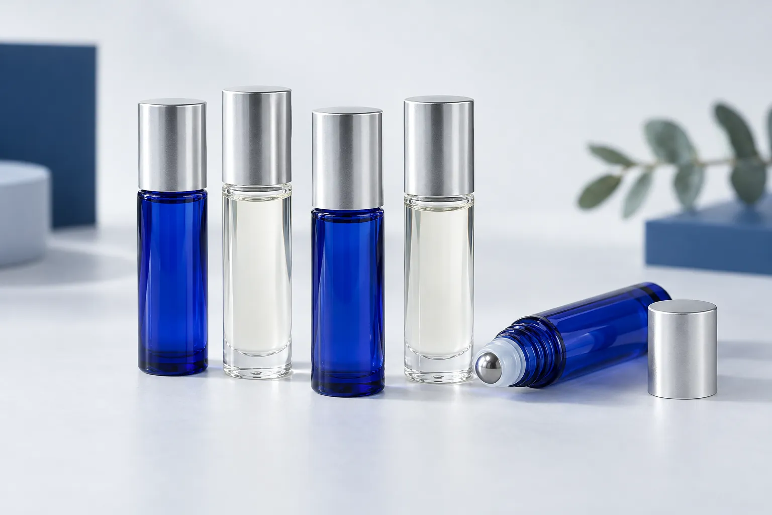Illustration of blank cobalt blue and clear glass roller bottles of perfume oil on a pale grey studio surface