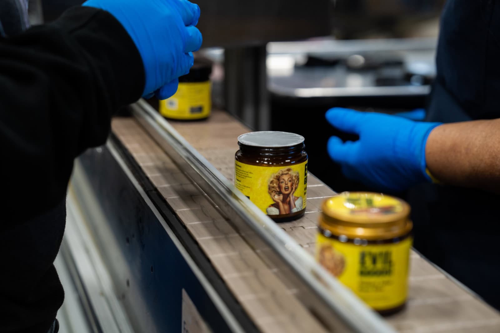 Gloved production workers handling filled and labelled amber tallow jars moving along the conveyor at Moe’s Group
